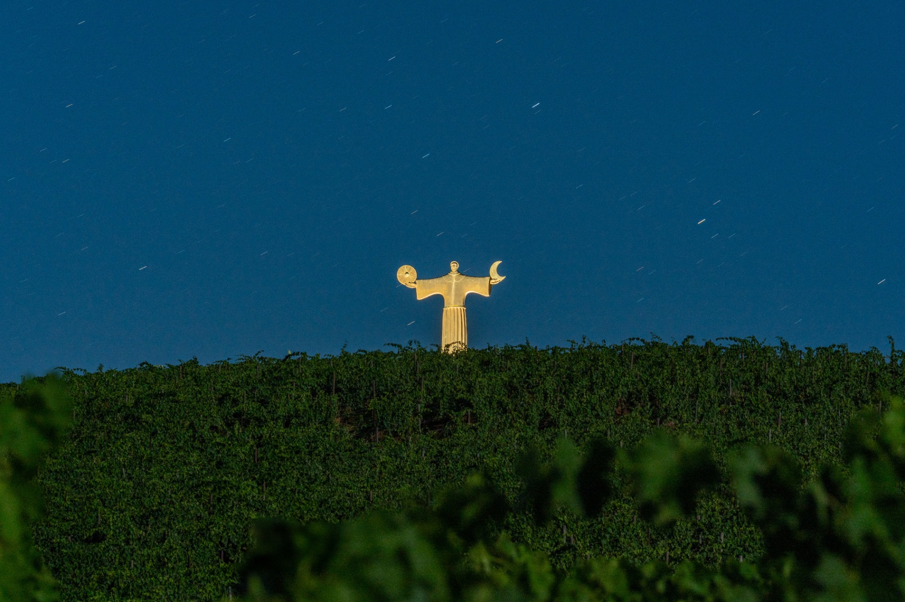 The golden Italo Zuffi sentinel sculpture on the vineyard ridge at dusk